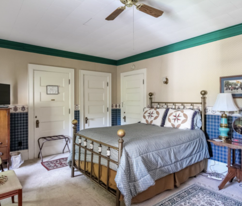 Cozy bedroom featuring a brass bed, patterned bedding, and a fan, with doors and a TV in a warm, inviting decor.