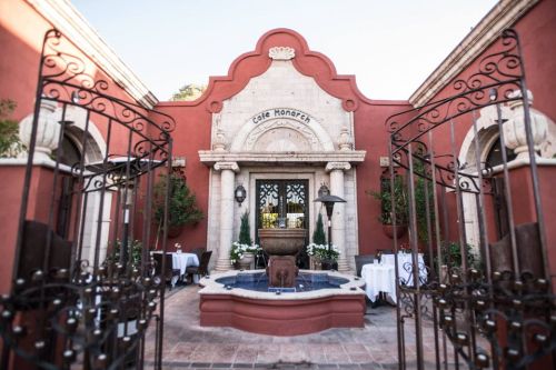Entrance of Café Monarch, featuring a decorative fountain and outdoor seating surrounded by lush greenery and ornate gates.