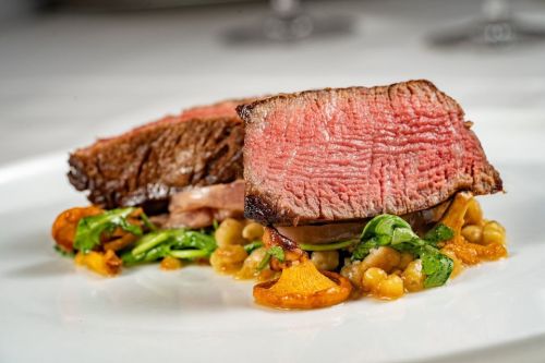 A plate featuring two slices of medium-rare beef on a bed of greens and garnished with mushrooms and grains.