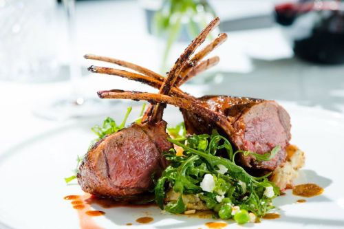 A gourmet dish featuring two lamb chops on a bed of arugula and mashed potatoes, garnished with sauce.