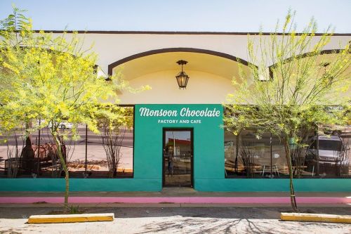 Exterior of Monsoon Chocolate Factory and Cafe, featuring a turquoise facade and yellow trees in front.