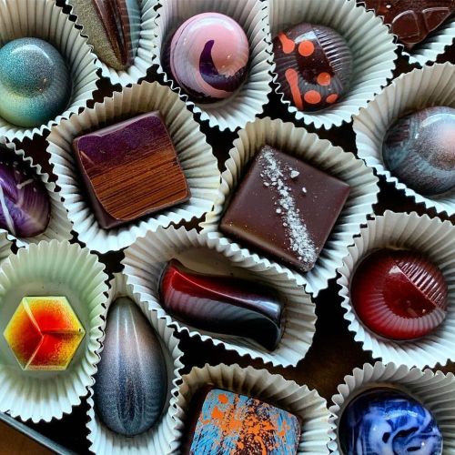 A variety of colorful, artistic chocolates arranged in paper cups, showcasing unique shapes and designs.