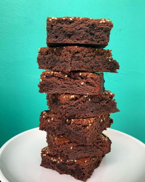 A stack of chocolate brownies with a textured surface, placed on a white plate against a bright turquoise background.