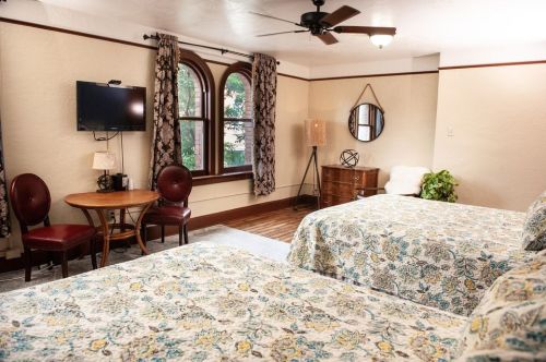 Cozy bedroom with two beds, a TV, a small table, and large windows, featuring floral bedding and warm decor.