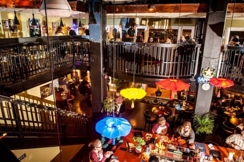 A vibrant restaurant interior with multiple levels, colorful hanging lights, and diners enjoying their meals.