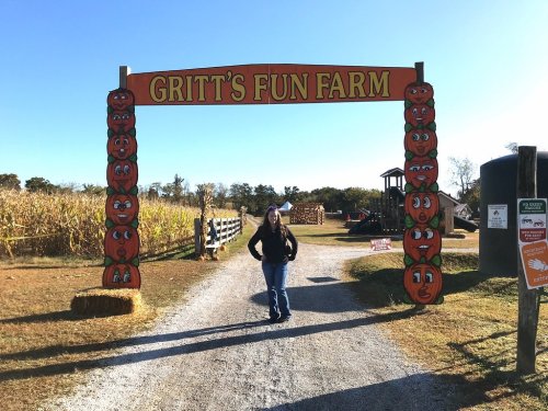 A person stands under a colorful sign reading "Gritt's Fun Farm," surrounded by pumpkin decorations and a cornfield.