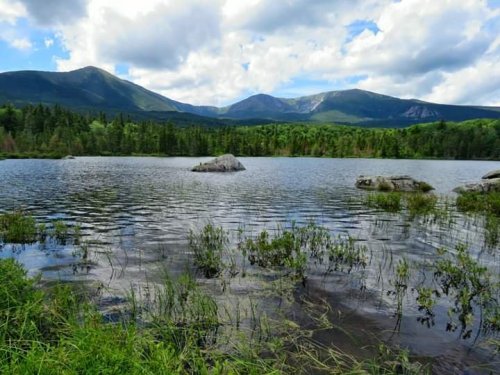 A serene lake surrounded by lush greenery and mountains under a partly cloudy sky.