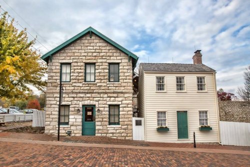 Two historic buildings side by side: one with a stone facade and green trim, the other white with green doors and windows.