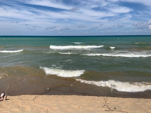 A sandy beach with gentle waves lapping at the shore under a partly cloudy sky.