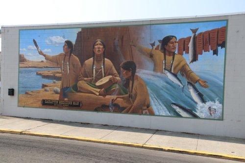 Mural depicting Indigenous figures engaged in traditional activities by a river, showcasing cultural heritage and connection to nature.