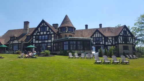 A large, historic mansion with a mix of black and white architecture, surrounded by green grass and outdoor seating.