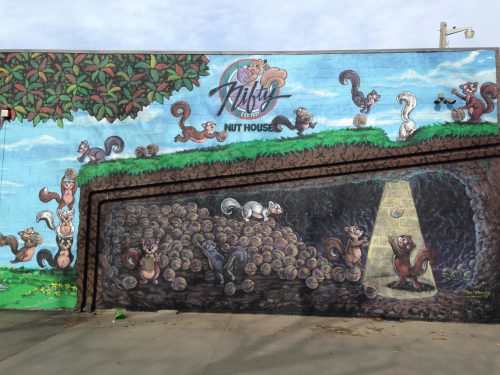 Colorful mural featuring playful squirrels around a pile of nuts, with a whimsical "Nutsy Nut House" sign above.
