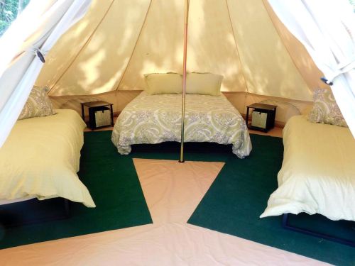 Cozy glamping tent with a double bed and two single beds, decorated with pillows and a green carpet.