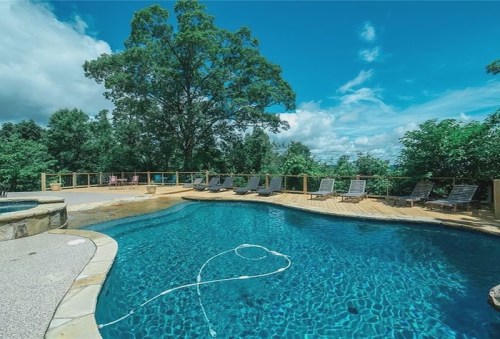 A serene pool surrounded by lounge chairs and lush greenery under a bright blue sky with scattered clouds.