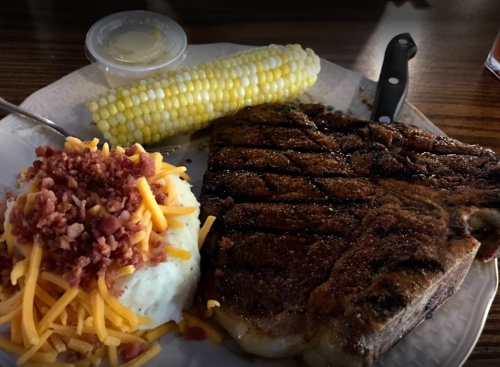 A plate featuring a grilled steak, corn on the cob, and mashed potatoes topped with cheese and bacon bits.