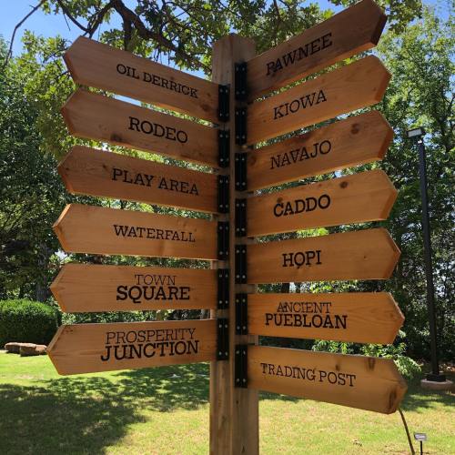 Wooden signpost with directional arrows pointing to various locations: Pawnee, Kiowa, Navajo, Caddo, and more.