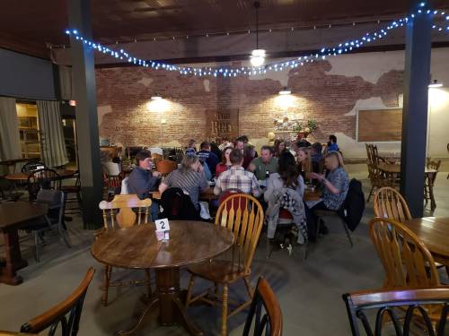 A cozy restaurant interior with diners at tables, brick walls, and string lights creating a warm atmosphere.