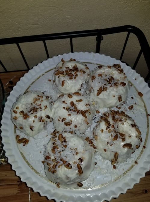 A white plate with six round desserts topped with coconut flakes and chopped pecans.