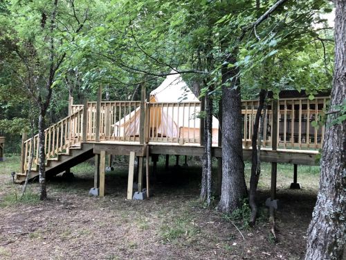 A wooden deck leads to a tent structure elevated among trees in a natural setting.