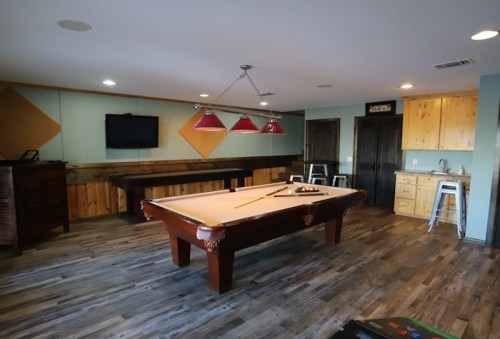 A spacious game room featuring a pool table, bar area, and modern decor with wooden accents.