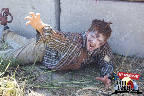A person in tattered clothing, covered in dirt and makeup, crawls on the ground, appearing distressed or frightened.