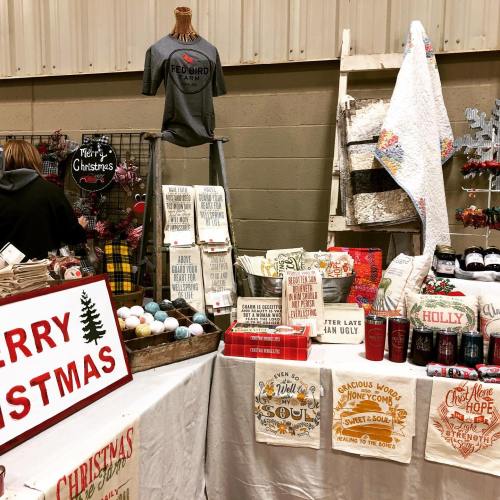 A festive market display featuring Christmas-themed items, including towels, decorations, and a holiday shirt.