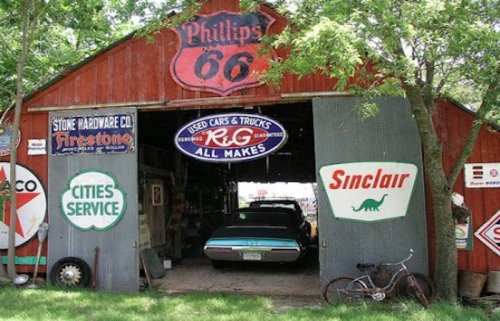 A vintage barn with classic gas station signs, showcasing a parked car and a bicycle outside.