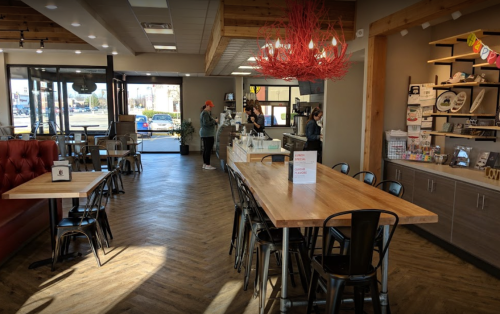 A modern café interior with wooden tables, a red light fixture, and customers ordering at the counter.