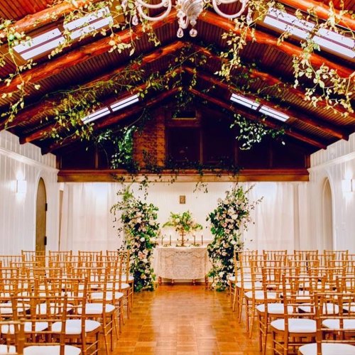 A beautifully decorated wedding venue with rows of chairs, floral arrangements, and a charming altar.