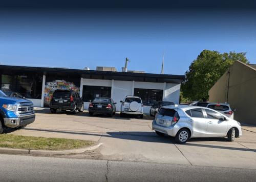 A parking lot with several cars in front of a modern building featuring colorful artwork on the wall.