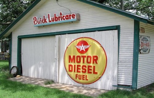 A vintage garage with a "Buick Lubricare" sign and a large "Motor Diesel Fuel" advertisement on the door.