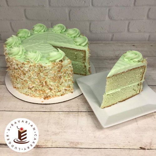 A round green cake with coconut flakes and decorative frosting, with a slice on a plate beside it.