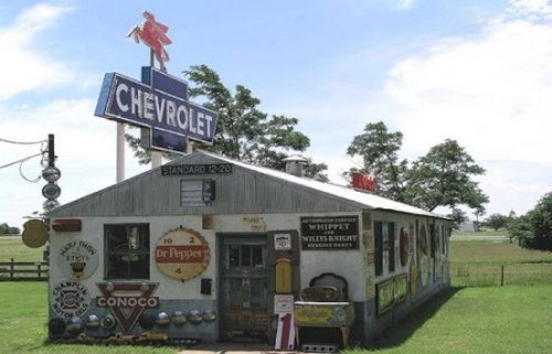 A vintage gas station with retro signs, including Chevrolet and Dr Pepper, set in a rural landscape.