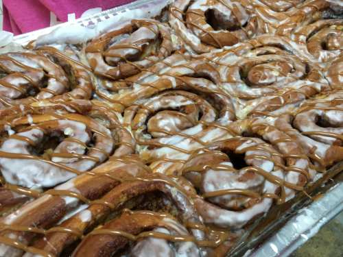 A tray of freshly baked cinnamon rolls drizzled with icing and caramel sauce.