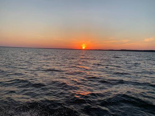 A serene sunset over a calm lake, with vibrant orange and pink hues reflecting on the water's surface.
