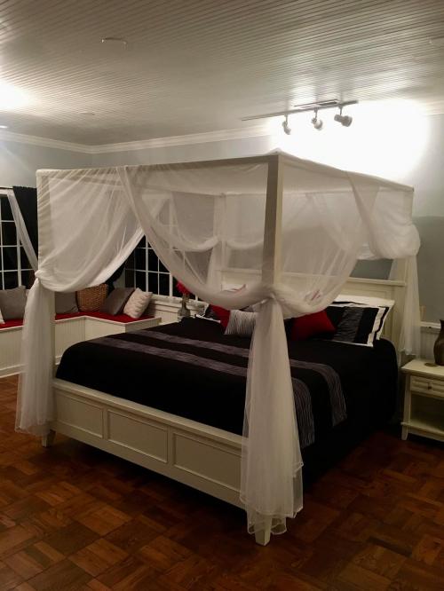 A cozy bedroom featuring a four-poster bed with white drapes, dark bedding, and decorative pillows.