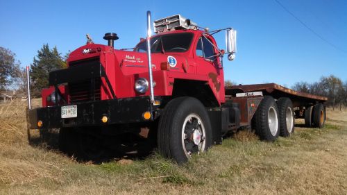 A vintage red truck with a flatbed trailer parked in a grassy field under a clear blue sky.