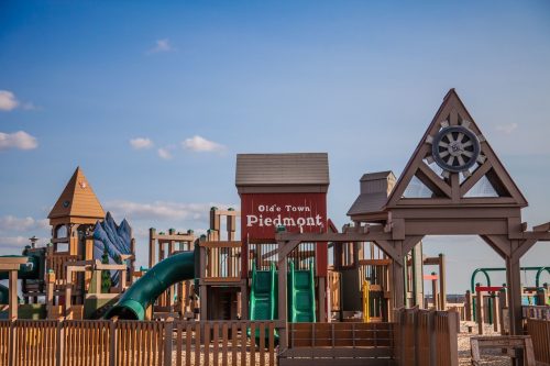 Colorful playground structure with slides and climbing features, featuring a sign that reads "Olde Town Piedmont."