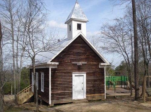 A rustic wooden building with a steeple, surrounded by bare trees and a playground in the background.