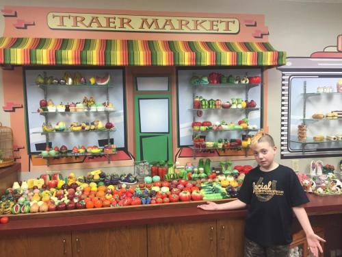 A child stands in front of a colorful display of artificial fruits and vegetables at Traer Market.