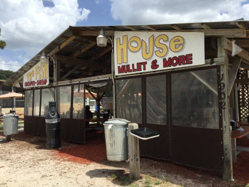 A rustic seafood shack with a sign reading "House Mullet & More," featuring outdoor seating and a casual atmosphere.