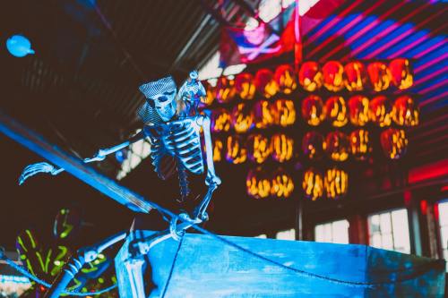 A skeleton figure stands on a boat, surrounded by colorful lights and hanging decorations in a festive setting.