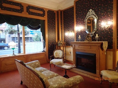 Cozy vintage living room with floral wallpaper, a fireplace, elegant furniture, and large windows.