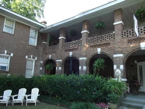 A brick house with a porch, featuring hanging plants and white Adirondack chairs in the garden.