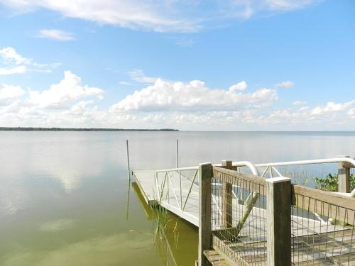 A serene lake view with a wooden dock extending into calm waters under a blue sky with fluffy clouds.