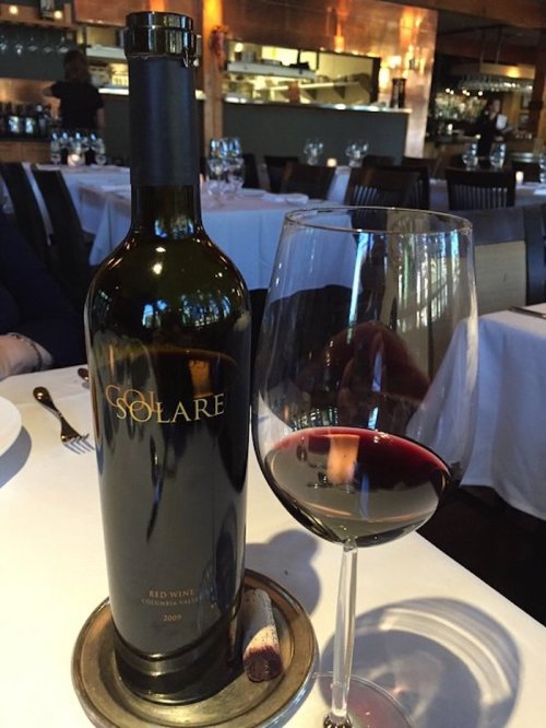 A bottle of Solare red wine next to a filled wine glass on a restaurant table.