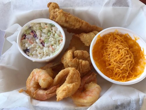 A plate featuring fried shrimp, coleslaw, and a side of cheese-covered dish, all served in a white container.