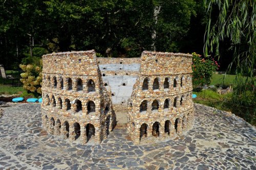A miniature stone replica of the Colosseum surrounded by greenery and a stone pathway.