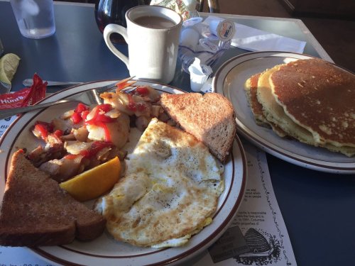 A breakfast plate with eggs, toast, pancakes, and fruit, alongside a cup of coffee on a blue table.