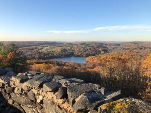 A scenic view of a lake surrounded by autumn foliage and rolling hills under a clear blue sky.